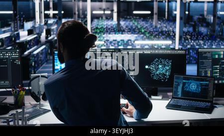 Computing facility computer scientist working with computer to track neural network working with AI large language model, while at work working with AI to oversee servers powering machine learning. Stock Photo
