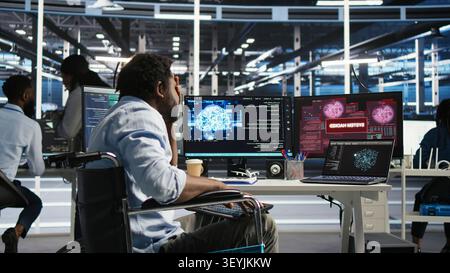 Man using a wheelchair in a data center reacts to a malware alert on a computer, securing server equipment and protecting confidential data. Stock Photo