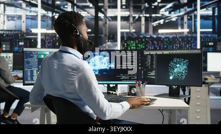 Server room employee talking in headset mic, coordinating technicians setting up hardware for AI deployment. Stock Photo