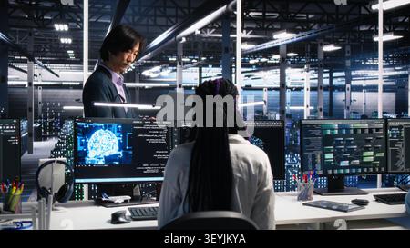 Team leader supervising technicians in server room working with AI to review infrastructure diagnostics. Stock Photo