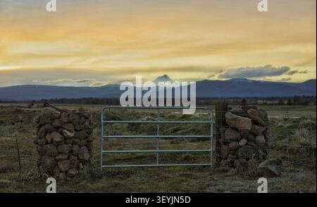 Rustic Farm Gate and Stone Pillars Opening to a Majestic Mountain Sunset View Stock Photo
