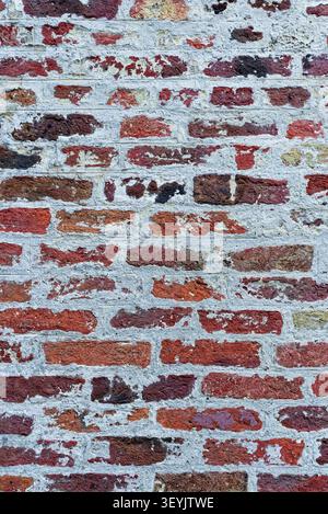 Full-frame red brick wall partly covered with worn white limewash, creating a distressed masonry background. Stock Photo