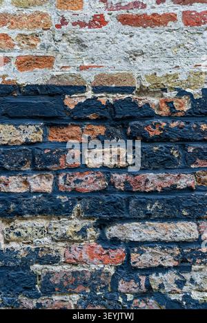 Full-frame old brick wall with white residue and dark tar-like staining, useful as a grunge background texture. Stock Photo