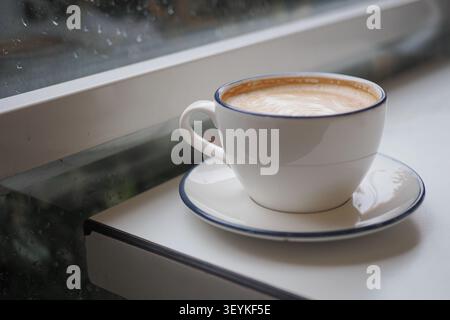 Coffee cup sits on table near window during rainy day Stock Photo