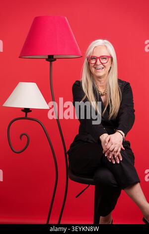 Senior woman smiling on a red background with lamp Stock Photo