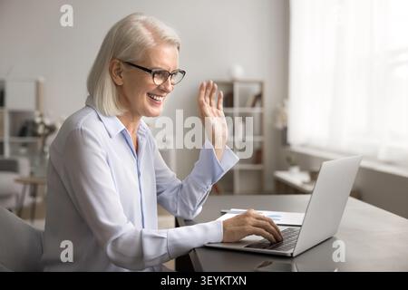 Smiling senior female accountant greeting client online using laptop webcam Stock Photo