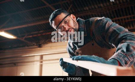 Carpentry, sanding or man in factory with wood, fabrication or quality control in furniture production. Below, ppe or carpenter with plank, timber Stock Photo
