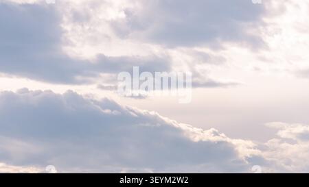 A wide view of an overcast sky with layered white and gray cumulus clouds in varying formations and a soft blue-gray tone throughout the frame. Stock Photo