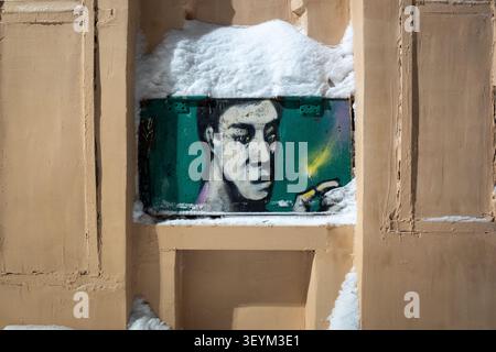 Weathered graffiti portrait of a man lighting a match painted on a beige urban wall, partially covered by fresh Stock Photo