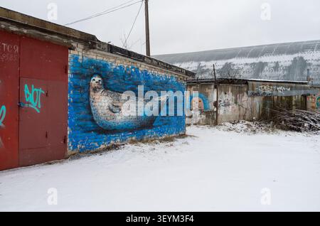 A large seal graffiti mural painted on a blue brick garage wall in a snowy, abandoned industrial area. Stock Photo