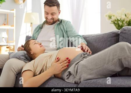Happy Family Couple Relaxing On Couch At Home, Expecting Baby Stock Photo