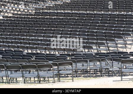 Hundreds of empty folding chairs are arranged in neat rows for a large outdoor event. The repeating pattern emphasizes scale and organization. Stock Photo