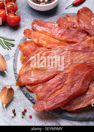 Spicy smoked dried turkey fillet with seasonings on slate board with cherry tomatoes, garlic and pepper Stock Photo