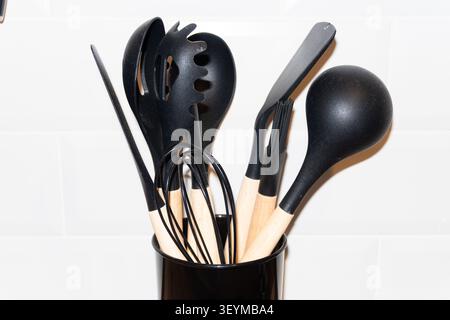 Set of modern black kitchen utensils with wooden handles on white ceramic tile wall background. High quality Stock Photo