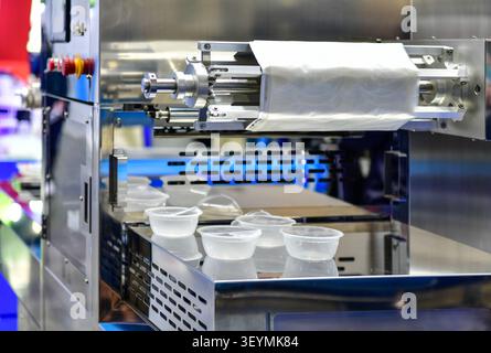 Automatic plastic tray sealing and packaging machine operating in food industrial factory Stock Photo