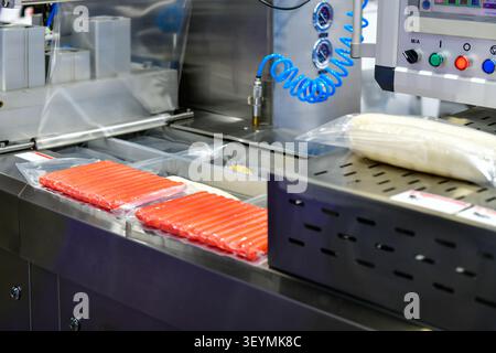 Automated vacuum packaging machine sealing fresh sausages on conveyor line in food processing factory plant Stock Photo