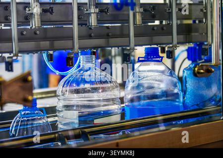 Automated water bottling machine filling large plastic bottles on conveyor belt in beverage production factory plant Stock Photo