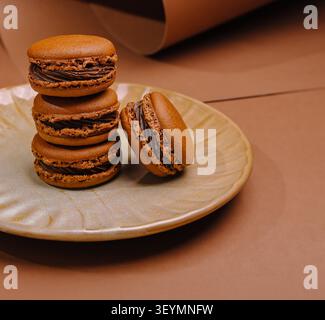 Chocolate macarons stacked on a decorative plate with one rolling off Stock Photo