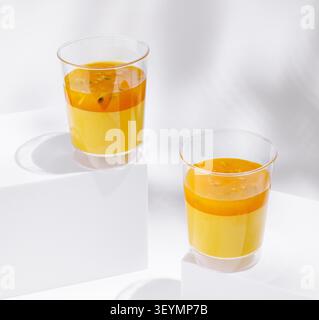 Two clear cups filled with colorful layered juice sit on a white surface. The drinks feature bright yellow and orange hues, creating an appealing visual display. Stock Photo