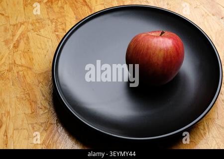 a red apple put in a black dish on brown wood table Stock Photo