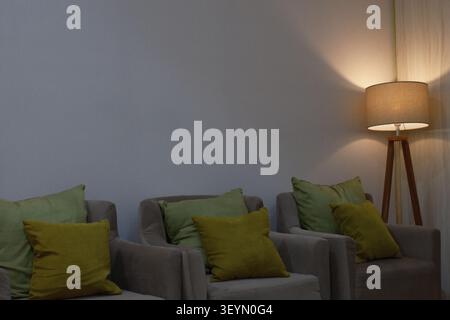 A room with three cushioned seats and a lamp with other amenities. Stock Photo