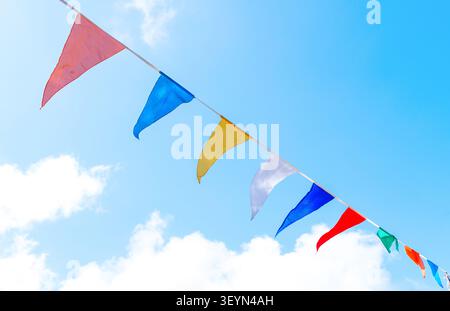 Vibrant triangular bunting flags sway gently on a string against a picturesque blue sky with soft white clouds during a festive celebration in Taxiarc Stock Photo