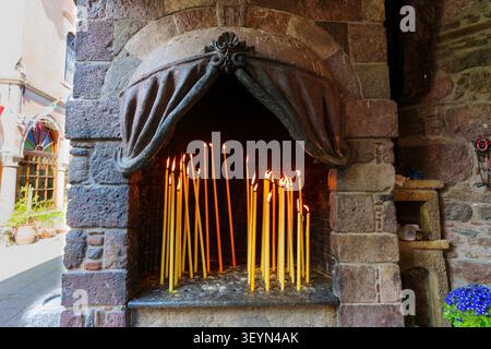 Golden votive candles burn brightly inside an ornate stone archway shrine at the historic Taxiarches Monastery in Lesbos, Greece, creating a peaceful, Stock Photo