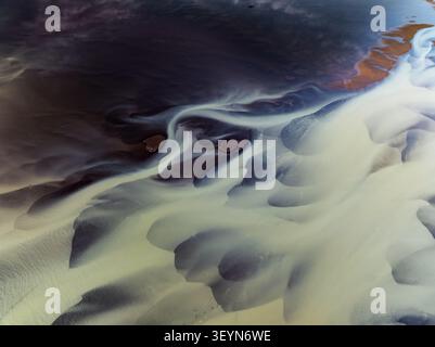 Aerial view of the intricate patterns of a glacial river delta with dark sediment and light-colored water flowing through the landscape of Iceland. Stock Photo