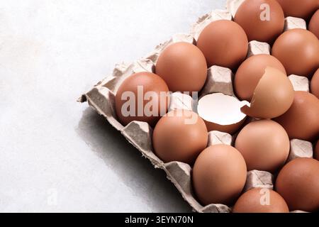 an opened empty cracked egg surround with full raw eggs in a tray on white background Stock Photo