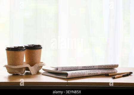 Two takeaway coffee cups with newspapers and pens on table Stock Photo