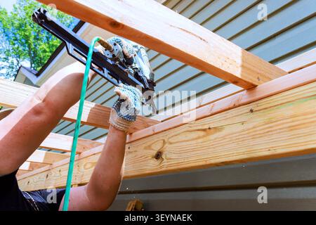 DIY worker constructs roof framing using air nail gun on wood structure outside Stock Photo