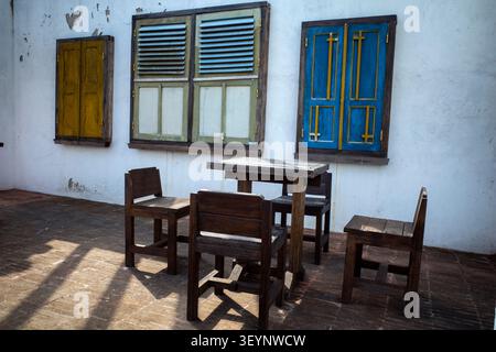 Rustic outdoor dining Set, a weathered wooden table with accompanying benches and chairs sits bathed in dappled sunlight, for outdoor gatherings Stock Photo