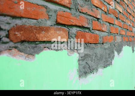 Red Brick Wall Under Construction with Grey Mortar, Industrial Masonry Work in Progress on Green Wall Background, Home Renovation and Building Structu Stock Photo