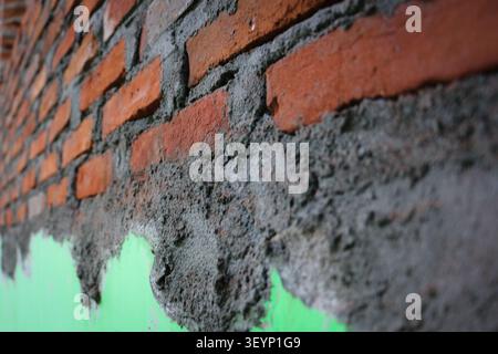 Red Brick Wall Under Construction with Grey Mortar, Industrial Masonry Work in Progress on Green Wall Background, Home Renovation and Building Structu Stock Photo