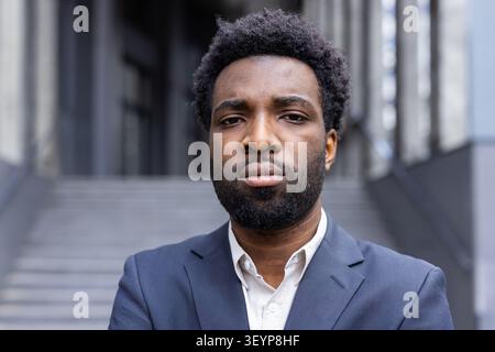 Young man wearing a business suit and beard standing outdoors, looking seriously at the camera, projecting confidence and professionalism in a modern urban setting Stock Photo