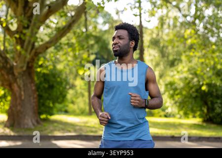 Athletic man running along a sunny park path, focusing on his outdoor workout while embracing a healthy lifestyle and staying active in green spaces Stock Photo