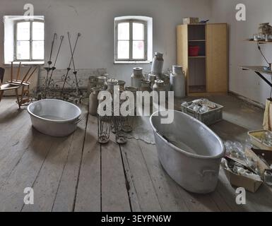 Old dusty milk cans, wrought-iron umbrella stands, two zinc pans and other sorted inventory stand salt witnesses of the past on a worn wooden floor in Stock Photo