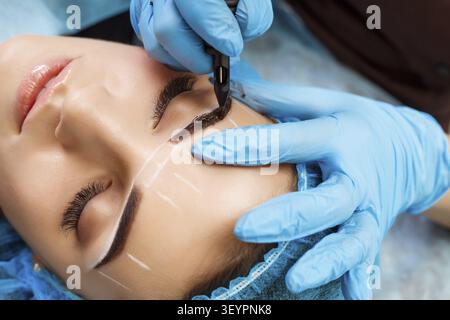 Cosmetologist applying permanent make up on eyebrows- eyebrow tattoo Stock Photo