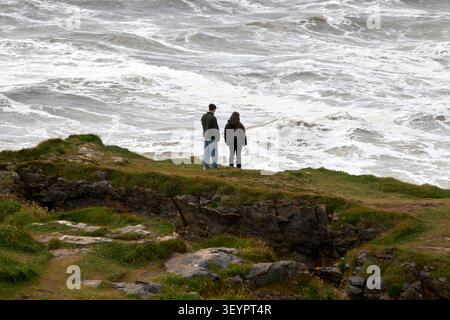 young couple standing on fairy bridges looking out to rough sea at rougey cliff walk near tullan strand county donegal republic  of ireland Stock Photo