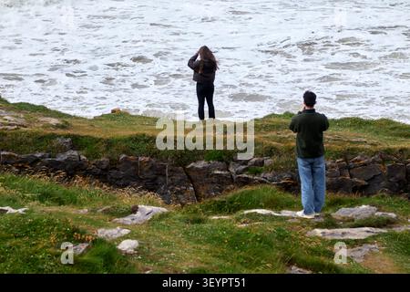 young man taking photos of young woman standing on fairy bridges at rougey cliff walk near tullan strand county donegal republic  of ireland Stock Photo