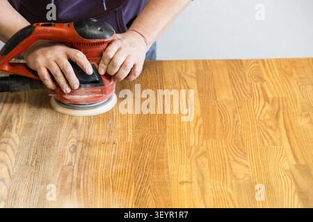 restoration of tabletop from elm wood - worker polishes surface of table using polishing machine Stock Photo