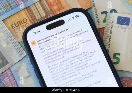 A smartphone on a background of Euro banknotes displays an official warning regarding fraudulent scam attempts issued the tax administration Stock Photo