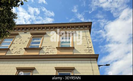 A low angle detailed shot reveals cracking beige stucco and damaged masonry on an old municipal structure featuring classical window crown moldings an Stock Photo
