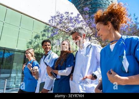 Diverse medical team walking together outdoors discussing healthcare Stock Photo