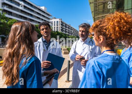 Diverse medical team collaborating outdoors near hospital building Stock Photo