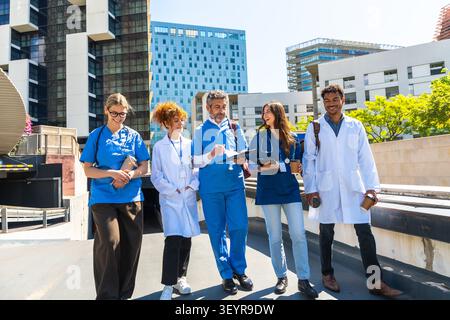 Diverse medical team walking and discussing outdoors near hospital building Stock Photo