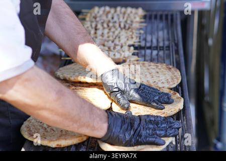 Experienced chef grilling fresh flatbreads on a large barbecue at a busy food stall during the Southsea Food Festival in Portsmouth, England. Stock Photo