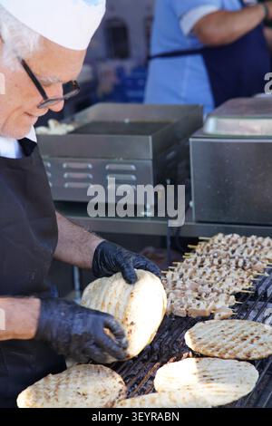 Experienced chef grilling fresh flatbreads on a large barbecue at a busy food stall during the Southsea Food Festival in Portsmouth, England. Stock Photo