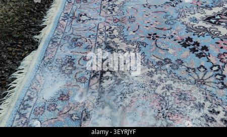 Foamy soap suds covering a portion of a patterned, blue and cream colored area rug during a cleaning process. Stock Photo