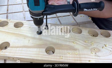 A close-up of a power tool drilling circular holes into a pine board, showcasing woodworking progress. Stock Photo